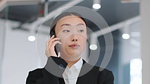 Mobile communication. Serious young asian woman manager talking with client or coworker via cellphone, free space