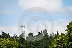 Mobile communications tower with antennas on top, showing above a forest tree line, sky and clouds in the background
