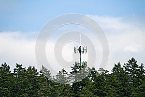 Mobile communications tower with antennas on top, showing above a forest tree line, sky and clouds in the background