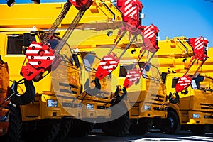 Mobile construction cranes with yellow telescopic arms and big tower cranes in sunny day