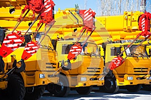 Mobile construction cranes with yellow telescopic arms and big tower cranes in sunny day