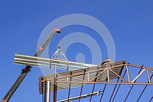 Mobile crane lifting metal roof sheet on palate truss up to stock above steel structure roof truss at the construction site