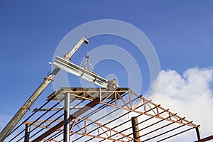 Mobile crane lifting metal roof sheet on palate truss up to stock above steel structure roof truss at the construction site