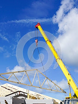 Mobile crane with yellow telescopic boom has lifted the wooden roof truss of the new building