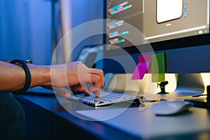 Mobile developer writes program code on a computer, typing on keyboard, programmer work in home office