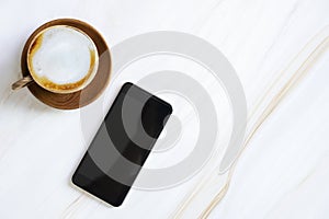 Mobile with empty screen with latte coffee cup on white marble table with free copy space. Business and technology