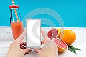 Mobile in female hands and citrus fruits on a blue background, oranges and grapefruits