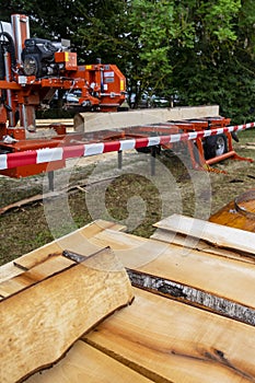Mobile industrial sawing machine on a truck trailer in operation when sawing logs, in the foreground are sawn boards on a pile