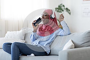 Mobile Karaoke. Joyful Black Muslim Woman Singing With Smartphone At Home