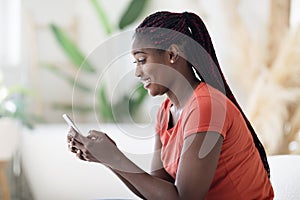 Mobile Messaging. Smiling Black Woman Using Smartphone While Resting At Home