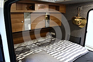 Mobile modern bedroom with wooden decorated shelves and cabinets above bed in trailer campervan BushCamp
