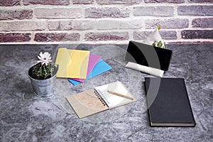 Mobile next to a blank notebook and a pencil next to a book and colored envelopes and a cactus on a table