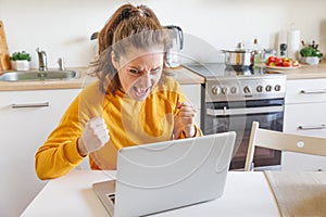 Mobile Office at home. Angry annoyed woman working using on laptop and screaming sitting in kitchen at home. Young stressed girl