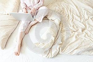 Mobile Office at home. Young woman in pajamas sitting on bed at home working using on laptop pc computer. Lifestyle girl studying