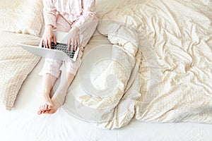 Mobile Office at home. Young woman in pajamas sitting on bed at home working using on laptop pc computer. Lifestyle girl studying