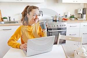 Mobile Office at home. Young woman sitting in kitchen at home working using on laptop computer. Lifestyle girl studying or working