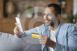 Mobile Payments Concept. Smiling Black Guy Using Smartphone And Credit Card