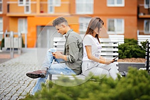 Mobile phone addiction concept - couple looking at their mobile phone while on a date sitting on the bench in city street