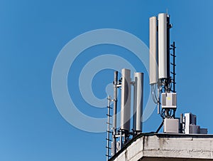 Mobile phone base station or cell tower atop of a building against a blue sky on a sunny day