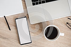 Mobile phone with blank empty white mockup screen, home office scene. Workplace, laptop computer, smartphone on office desk