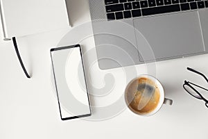 Mobile phone with blank empty white mockup screen. Workplace, laptop computer, smartphone on office desk