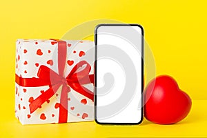 mobile phone with blank screen on colored background with hearts, calendar and gift box, valentine day concept