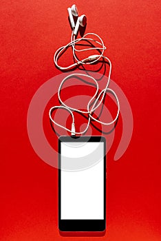 Mobile phone with blank screen and headphone on red background. Top view