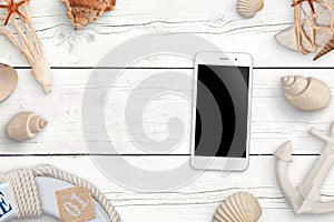 Mobile phone with blank screen for mockup on white wooden table surrounded with shells