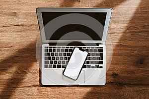 Mobile phone with blank white mockup touchscreen and laptop computer on office desk, top view