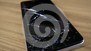 A mobile phone with a broken screen lies on a table