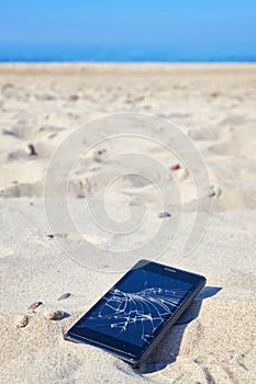 Mobile phone with broken screen in sand on a beach.