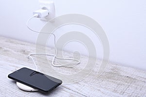 Mobile phone charge on a wireless charger, modern equipment concept on a wooden table background