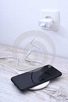 Mobile phone charge on a wireless charger, modern equipment concept on a wooden table background