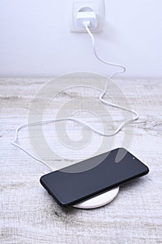 Mobile phone charge on a wireless charger, modern equipment concept on a wooden table background