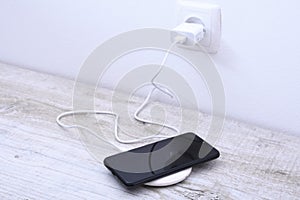 Mobile phone charge on a wireless charger, modern equipment concept on a wooden table background