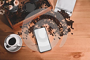 Mobile phone, coffee cup and roasted coffee beans on wooden table.