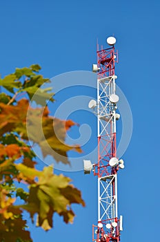 Mobile phone communication radio tv tower, mast, cell microwave antennas and transmitter against the blue sky and trees