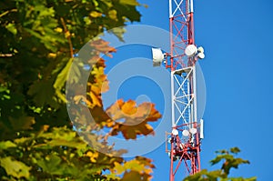 Mobile phone communication radio tv tower, mast, cell microwave antennas and transmitter against the blue sky and trees