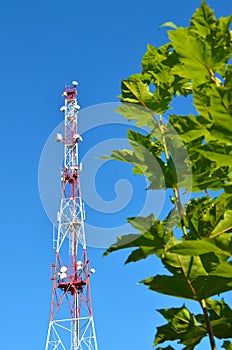 Mobile phone communication radio tv tower, mast, cell microwave antennas and transmitter against the blue sky and trees
