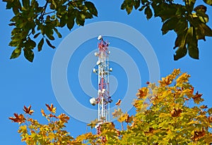 Mobile phone communication radio tv tower, mast, cell microwave antennas and transmitter against the blue sky and trees