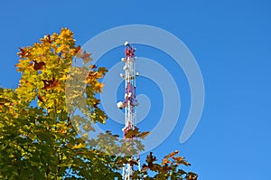 Mobile phone communication radio tv tower, mast, cell microwave antennas and transmitter against the blue sky and trees