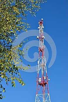 Mobile phone communication radio tv tower, mast, cell microwave antennas and transmitter against the blue sky and trees