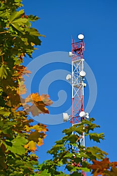 Mobile phone communication radio tv tower, mast, cell microwave antennas and transmitter against the blue sky and trees