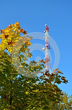 Mobile phone communication radio tv tower, mast, cell microwave antennas and transmitter against the blue sky and trees