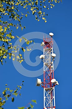 Mobile phone communication radio tv tower, mast, cell microwave antennas and transmitter against the blue sky and trees