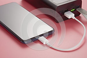 A mobile phone connected by a cable to a power bank. Pink background