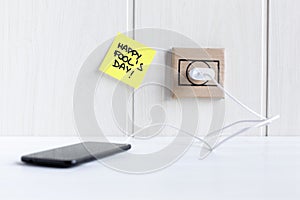 Mobile phone connected to a cardboard plug next to a sticky note with the phrase