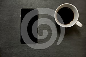 Mobile phone and cup of coffee - on dark slate