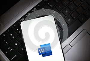 Mobile phone displaying Microsoft Word logo on laptop keyboard background illustrative editorial technology