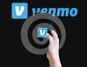 Mobile phone displaying Venmo app logo with hand holding device illustrative
